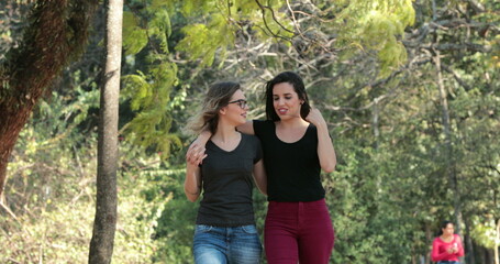 Two girlfriends together walking at the park embracing each other