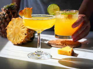Summer cocktail drink with fresh pineapple and lime, female bartender hand in background.