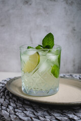 Close up of a mojito cocktail in a lowball glass with ice, fresh mint, and lime