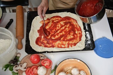 Top view. Process of preparing pizza. Chef pours tomato sauce over the rolled dough. Fresh ingredients on kitchen table