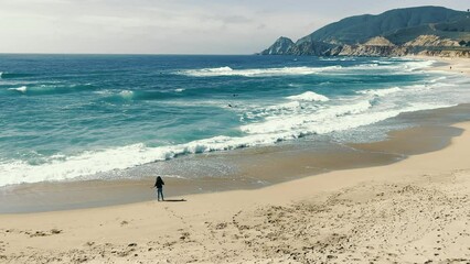 A girl standing on the shore of a sandy beach of the Pacific Ocean. Big waves come to the shore. Sunny day.