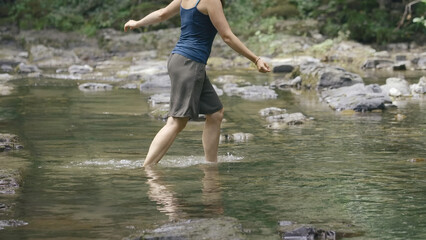 Woman walks in river water. Creative. Beautiful woman barefoot crosses mountain river. Woman went into river water while relaxing in green forest