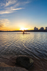 Landscape of sunset with clouds over the pond in the city and a canoeing man