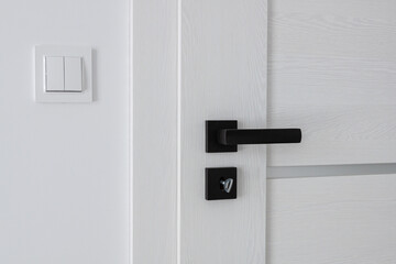 Closed white wooden door with black metal handle and key. Close-up of door handle and interior fittings.