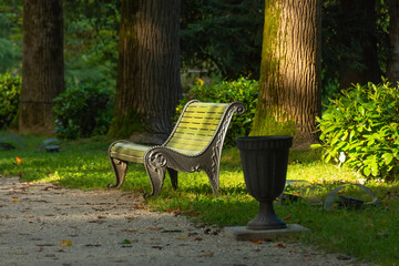 Wooden green bench with a metal base with a nearby urn in a shady park.