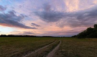 Fototapeta na wymiar Purple clouds in the sunset sky. The country road goes beyond the horizon. Evening landscape.