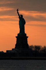 Silhouette of Statue of Liberty against a vivid orange sunset sky concept for NYC landmarks, American patriotism and symbol of freedom in America