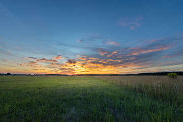 Rural landscape with colorful clouds and sun on the horizon. Bright sunset.