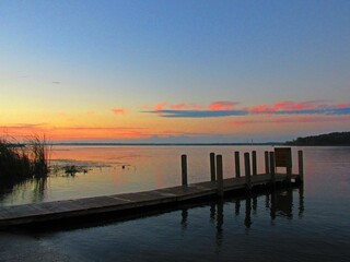 Obraz premium An orange sunrise remains in a blue sky over a dock on Michigan's Muskegon Lake