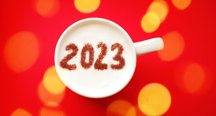 2023 on coffee foam. Cup of Cappuccino top view. Festive glowing. New Year banner