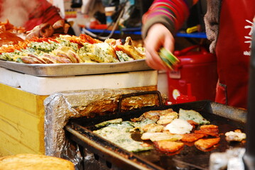 Night food market in South Korea, Seoul with woman cooking on grill.