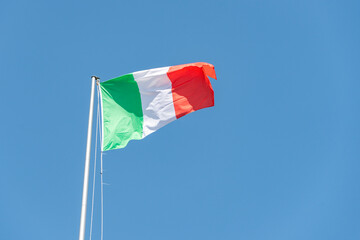 Italian flag waving in the wind. Tricolour flag: red, white and green fluttering in a brisk breeze against a bright blue sky. - 521077669