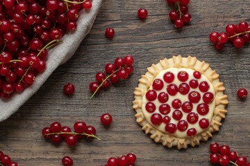 rote Johannisbeeren und Pudding in Törtchen auf Tisch aus Holz