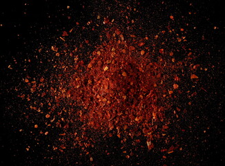 Fototapeta na wymiar Spicy chili pepper flakes, crushed, milled dry paprika pile on black, top view