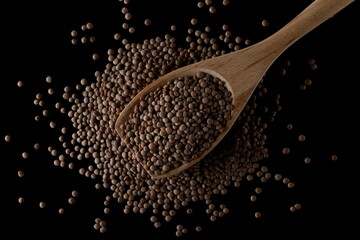Brown uncooked lentils in wooden spoon isolated on black