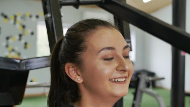 face of a beautiful smiling middle eastern woman with gray eyes and lush eyelashes exercising in the gym on a simulator lifting weights with her hands