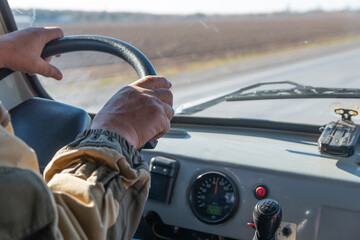 Man hands on the steering wheel of an old SUV . There are road ahead and steppe behind the windshield.