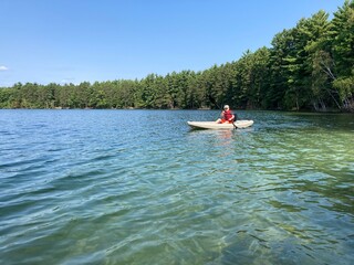 Boy paddles kayak in a pristine or clear lake surrounded by forest