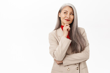 Image of stylish senior asian woman in suit, smiling and looking intrigued, thoughtful face...
