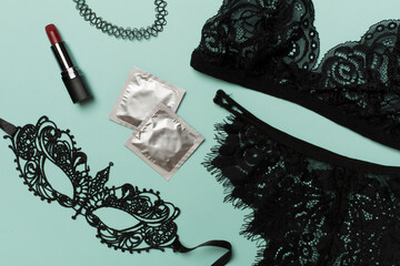 Lace mask, lingerie and condoms on color background, top view