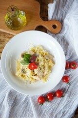 Italian cuisine. Pasta with cheese and white poultry meat. Served in a white plate on a wooden board next to red tomatoes.