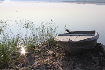 an empty gray metal boat on the shore of a lake, a river, near reeds and among stones, the sun is reflected in the water, creating sun bunnies