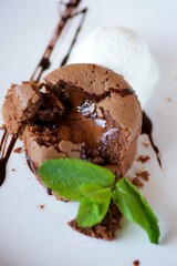 A cupcake or pancake with chocolate filling lies on a plate of ice cream. The dish is decorated for serving