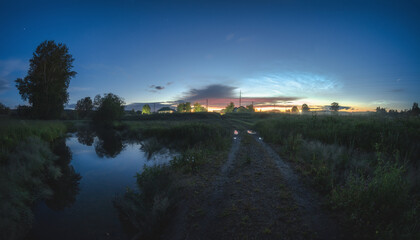 Nightscape with river, road, village and noctilucent clouds at summer white night