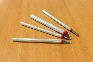 Various sharp precision craft knives with different blades on a lacquered wooden surface