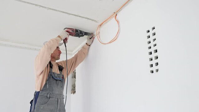 The master builder drills a hole in the wall during the repair work in the room. Recovery and restoration of the room. A male electrician drills a track in a concrete wall for laying a cable.