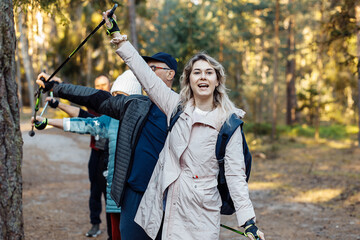 Group joyful people hold together Nordic trekking poles in air on trek while hiking in forest....