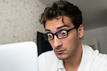 Obraz premium Close up portrait of shocked man with bugged eyes looking at laptop