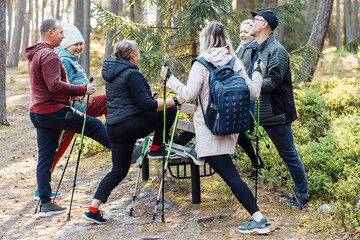 Group people learning to make Nordic walking with trekking sticks in forest, stand one leg on...