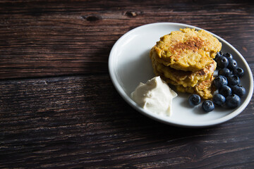 Apple pancakes with sour cream and blueberries on a white plate on a wooden table