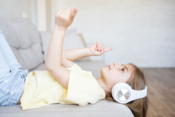 kid girl lying upside down on couch at home, listening music in earphones. 