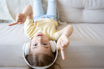 School child girl listening loud music in wireless earphones at sofa in living room.