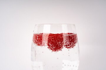 Close up of a wineglass filled with sparkling water and raspberries