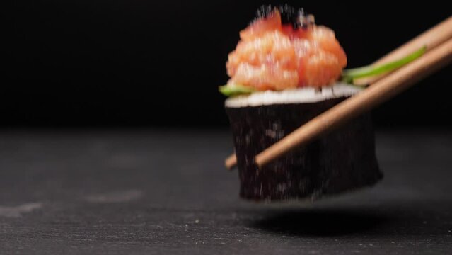 Take one sushi roll from black slate board using chopsticks, Closeup