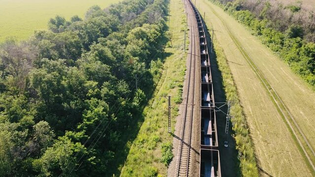 Cargo bulk carrier train transporting wagons across rural landscape, aerial view