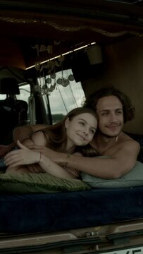 A young couple in love admiring the views and cuddling in bed inside a camper 