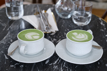 A cup of matcha latte is on the table in a cafe. Delicious green matcha tea in a green cup close-up. Japanese hot milky beverage. Healthy Matcha Tea Made with Organic Ingredients
