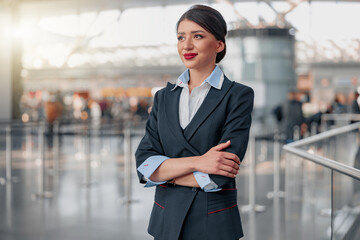 Beautiful stewardess with arms crossed looking away in airport terminal