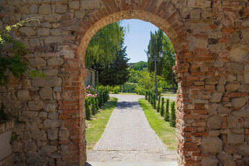Fototapeta na wymiar Brickstone arch and passage in Fortunago, one of the most charming villages of Oltrepò Pavese, Lombardia countryside, Italy. Green park in the background.