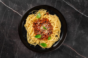 Delicious mouth-watering classic Italian spaghetti pasta with tomato sauce, parmesan cheese and basil on a plate on a dark table. Top view, horizontal