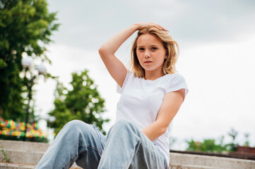 Obraz premium Portrait of a teenage girl in casual clothes in the park. Summer skateboarding, active lifestyle. A student or a schoolboy is sitting on a skateboard during the summer holidays. Sports recreation.