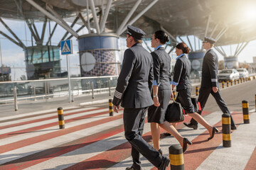 Two flight attendants and male pilots walking in a row while crossing the road