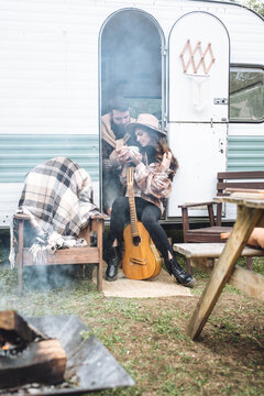 Young beautiful loving couple travelling across country in the van. Millennial man and woman in a travel camper. Cozy atmosphere, vacations vibe. Playing guitar, drinking tea, cooking on a campfire