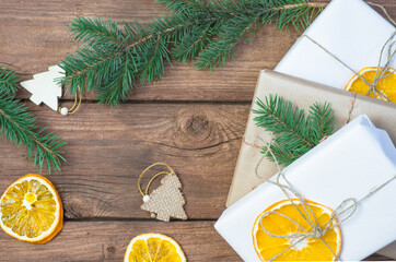 Fototapeta na wymiar Christmas presents or gift box wrapped in kraft paper with decorations, pine cones, dry orange orange slices and fir branches on a rustic wooden background. Holiday concept