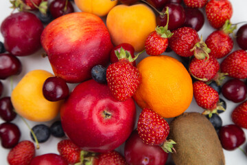 Different ripe fruits and berries lie in a solid layer on the white. High quality photo
