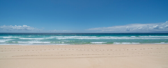 Fototapeta na wymiar Minimalist seascape panorama with footsteps on the beach against blue sea, waves and clear sky.
